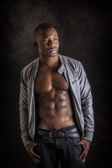 Wall Mural - Handsome shirtless muscular black young man's with jacket open on naked torso, looking at camera, on dark background in studio shot