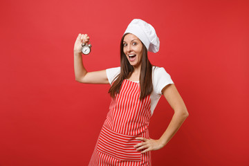 Housewife female chef cook or baker in striped apron, white t-shirt, toque chefs hat isolated on red wall background. Smiling woman hold in hand retro alarm clock hurry up. Mock up copy space concept.