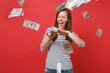 © ViDi Studio - Crazy woman in striped clothes screaming scattering throwing out money banknotes lots of dollars isolated on bright red wall background. People sincere emotions, lifestyle concept. Mock up copy space.