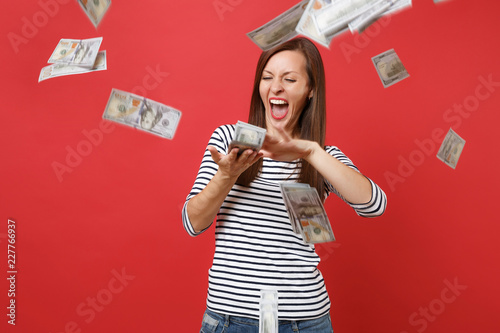 Cuadros en Lienzo Crazy woman in striped clothes screaming scattering throwing out money banknotes lots of dollars isolated on bright red wall background