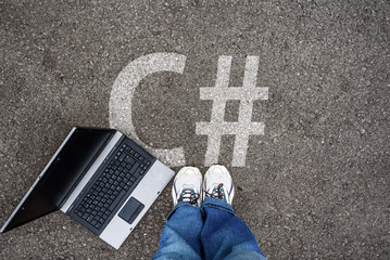 man legs in sneakers standing next to laptop and c sharp, c# on asphalt
