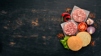 Raw burger Cooking a burger with meat. On a black wooden background. Top view. Free copy space.