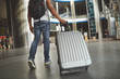 Low angle of a plastic silver luggage carried by a man who is hurrying up not to miss his flight
