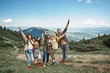 © Yakobchuk Olena - Full length portrait of four women and man standing jointly on ascent to peak. They hugging and lifting arms displaying peaceful and greeting gestures