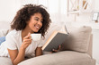 © Prostock-studio - Happy woman drinking tea and reading book on couch