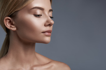 Peaceful young woman standing against the grey background and thoughtfully looking down