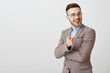 Your ideas promising. Pleased and delighted smart businessman in trendy formal jacket and glasses smiling and pointing at camera as if agreeing and liking interesting plan over gray background