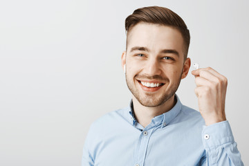 Wall Mural - Close-up shot of happy optimistic and friendly young handsome guy with beautiful smile and bristle taking off wireless earbud answering question being interrupted from listening favorite track