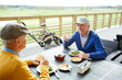 © pressmaster - Two mature golf players sitting by table in front of one another, having salad and tea and discussing the last game