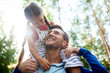 © pressmaster - Happy young man with toothy smile looking at little daughter on his shoulders during chill in the forest