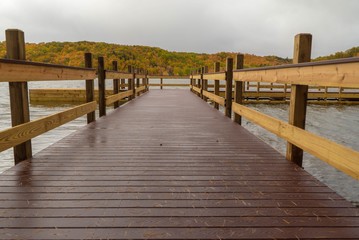 Wall Mural - Dramatic closeup view from the end of a dock on a lake with colorful Autumn landscape in background