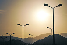 High-speed Road Highway With City Lighting Poles Lamps. High Mountains In The Fog Against The Background, Sunset, Twilight, Landscape, Aerial Perspective, Cars