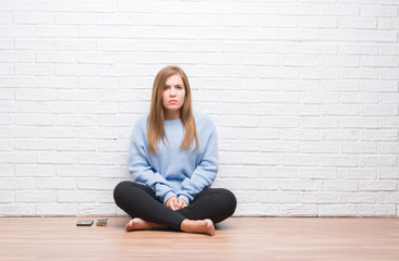 Sticker - Young adult woman sitting on the floor in autumn over white brick wall skeptic and nervous, frowning upset because of problem. Negative person.