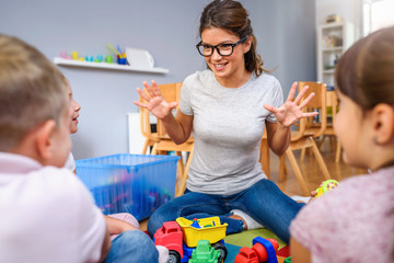 Preschool teacher talking to group of children sitting on a floor at kindergarten