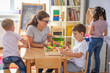 © lordn - Preschool teacher with children playing with colorful wooden didactic toys at kindergarten