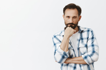 Wall Mural - I am not sleeping. Tired and bored funny adult male with beard, closing one eye and gazing with indifferent exhausted expression at camera, leaning on fist while being sleepy, naping on meeting