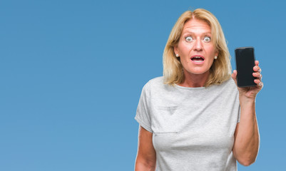 Canvas Print - Middle age blonde woman showing blank screen of smartphone over isolated background scared in shock with a surprise face, afraid and excited with fear expression