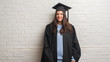 © Krakenimages.com - Young brunette woman standing over white brick wall wearing graduate uniform with a happy face standing and smiling with a confident smile showing teeth