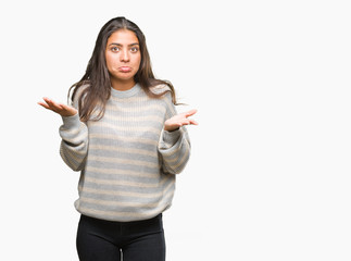 Poster - Young beautiful arab woman wearing winter sweater over isolated background clueless and confused expression with arms and hands raised. Doubt concept.