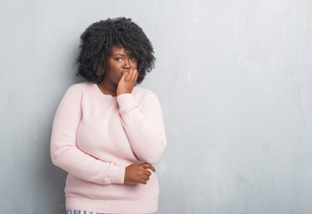 Canvas Print - Young african american plus size woman over grey grunge wall wearing winter sweater looking stressed and nervous with hands on mouth biting nails. Anxiety problem.