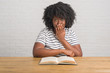 Young african american woman sitting on the table reading a book cover mouth with hand shocked with shame for mistake, expression of fear, scared in silence, secret concept
