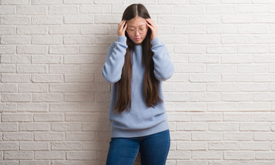 Poster - Young Chinise woman over white brick wall with hand on head for pain in head because stress. Suffering migraine.