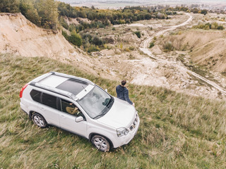 white suv at the top of the hill in autumn overcast weather. man standing near car around wild nature