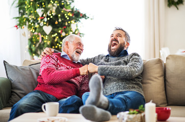 Poster - A senior father and adult son sitting on a sofa at home at Christmas time, laughing.