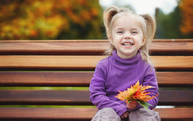 Portrait of a smiling little girl. She is holding in her hand a bouquet of autumn colorful leaves