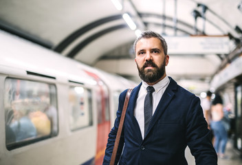 Hipster businessman with a bag waiting for the train in subway.