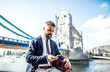 Hipster businessman with smartphone sitting by the Tower Bridge in London.