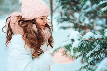 Winter Portrait Of Happy Kid Girl In White Coat And Pink Hat And Mittens Playing Outdoor In Snowy Winter Forest With Snow Covered Fir Branch. Traveling, Vacation And Active Winter Holidays Concept
