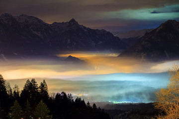 Wall Mural - Beautiful winter night view of the city Brand in the valley of the Brandnertal in the mountains of the Alps in Vorarlberg, Austria, with illuminated fog clouds