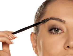 Young woman contouring her eyebrows with dry brush on white background