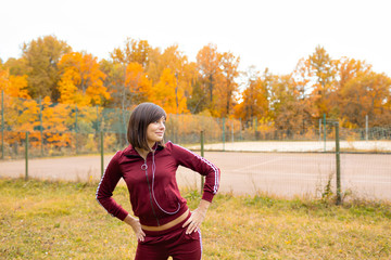 Portrait of young woman in fall forest. Brunette woman in autumn park makes a run and warm up. Sports lifestyle