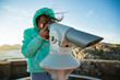 © Suzi Media  - Teenage girl stands on rocky northern seashore, looking through touristic telescope, exploring the coastal rocks. Travel and enjoy adventure in Norway. Beautiful view of fjord and mountains in sunset