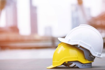 yellow and white hard safety wear helmet hat in the project at construction site building on concrete floor on city with sunlight. helmet for workman as engineer or worker. concept safety first. 