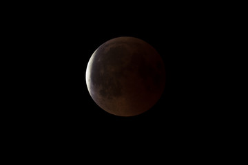 Wall Mural - super bloody moon, full eclipse end phase against black sky background, earth's shadow starting to m
