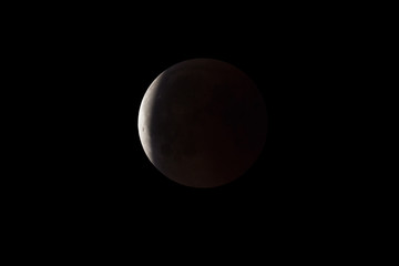 Wall Mural - super bloody moon, full eclipse end phase against black sky background, earth's shadow starting to m