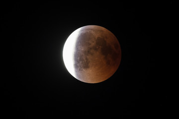 Wall Mural - super bloody moon, full eclipse end phase against black sky background, three-quarters of the moon s