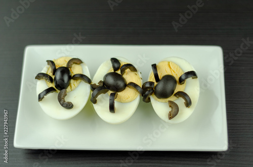 Fotografía funny snack with olive spiders on egg halves for halloween party, creative food