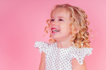 little girl beauty queen blue eyes, curls blonde hairstyle with a tiara crown on her head in a cute white dress in peas posing in the studio on a pink background.birthday celebration,Beauty contest