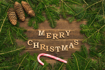 Inscription Merry Christmas on a wooden background. Frame of fir branches, lollipop stick.