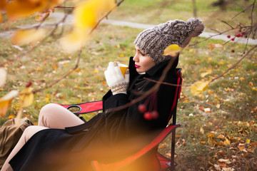 Portrait of a beautiful and dreamy girl in a chair with a cup of coffee in the autumn