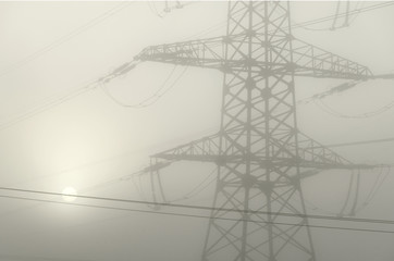 View of the part of the tower supporting the high-voltage line in the fog. Through the fog visible solar circle. Background. Black and white.