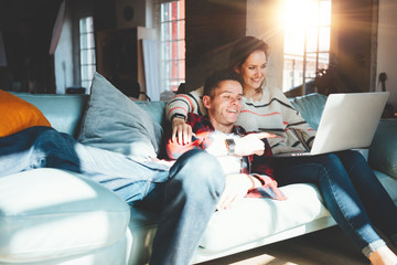 Lovely young couple at home. Happy man and woman sitting on the couch together and watching TV series on laptop. Bright loft apartment