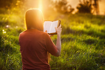 Girl reading the Bible at sunset