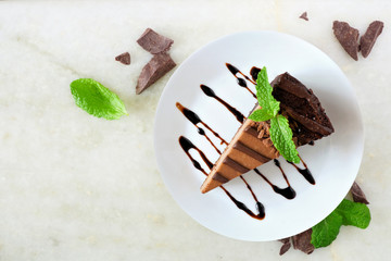 Poster - Slice of chocolate cheesecake on plate, above view over a white stone background