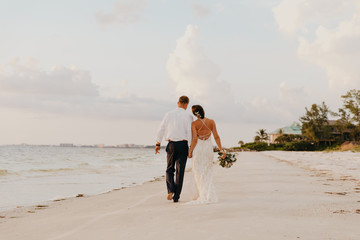 perfect sunset destination beach wedding with beautiful bride and groom walking down the coastline