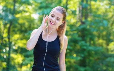 Wall Mural - Athletic young woman with headphones on a bright summer day in the forest